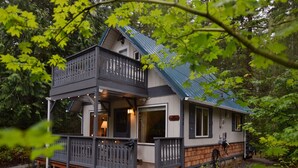 Une cabane à deux étages dotée d’un balcon, entourée d’arbres.
