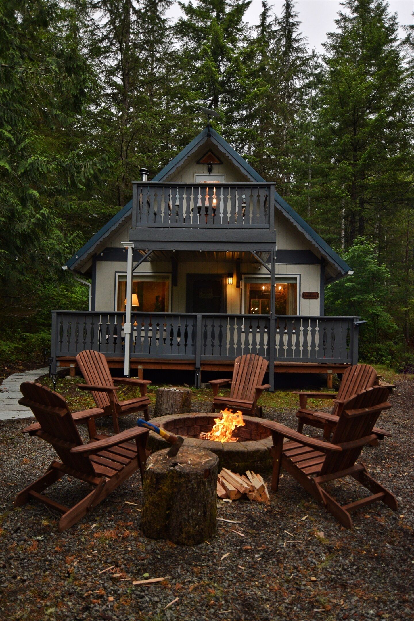 A cabin with a balcony, wooden chairs, and a fire pit.