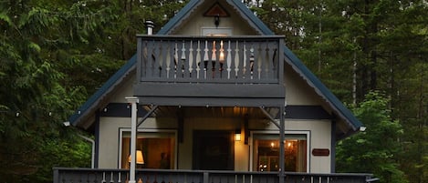 A cabin with a balcony, wooden chairs, and a fire pit.