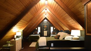 Une chambre confortable située sous les toits, avec des poutres apparentes, deux lits, des lampes de chevet et une petite table agrémentée d’une plante.