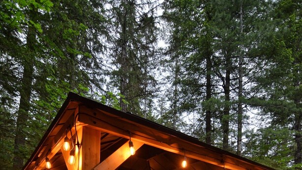 Un belvédère en bois agrémenté de guirlandes lumineuses, une terrasse en bois et un banc.