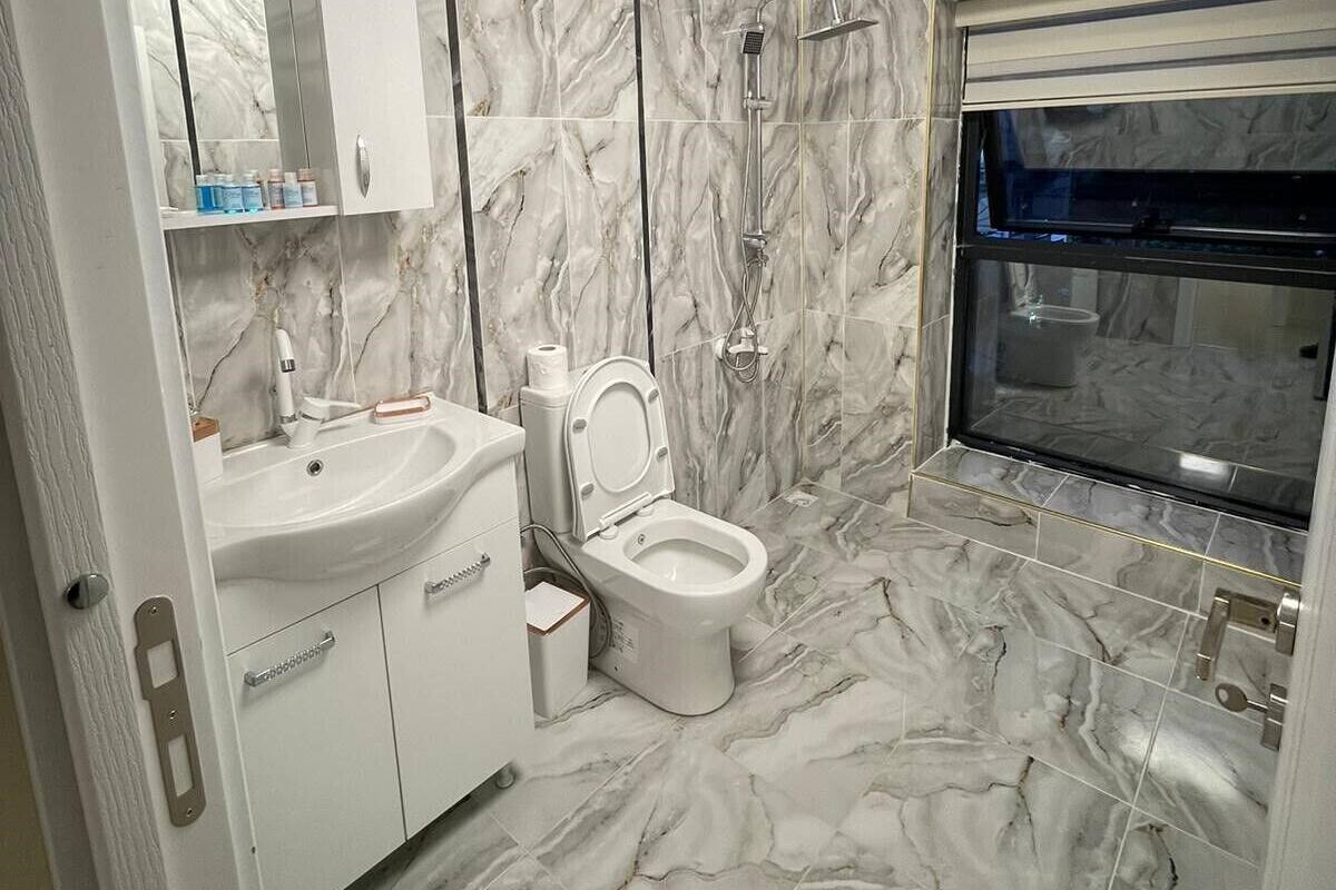 A bathroom with a marble floor, a toilet, a sink, and a shower.