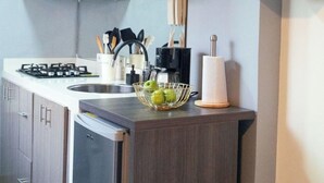A modern kitchen with a built-in stove, a sink, and a refrigerator. There is a wooden cabinet above the stove and a vase with flowers on a shelf to the right. - Reyes House Bogotá (Bogotá)