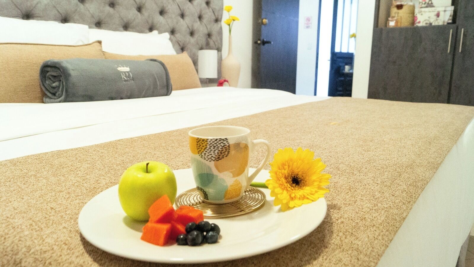 A breakfast tray with an apple, a cup of coffee, and a flower on a hotel room table.
