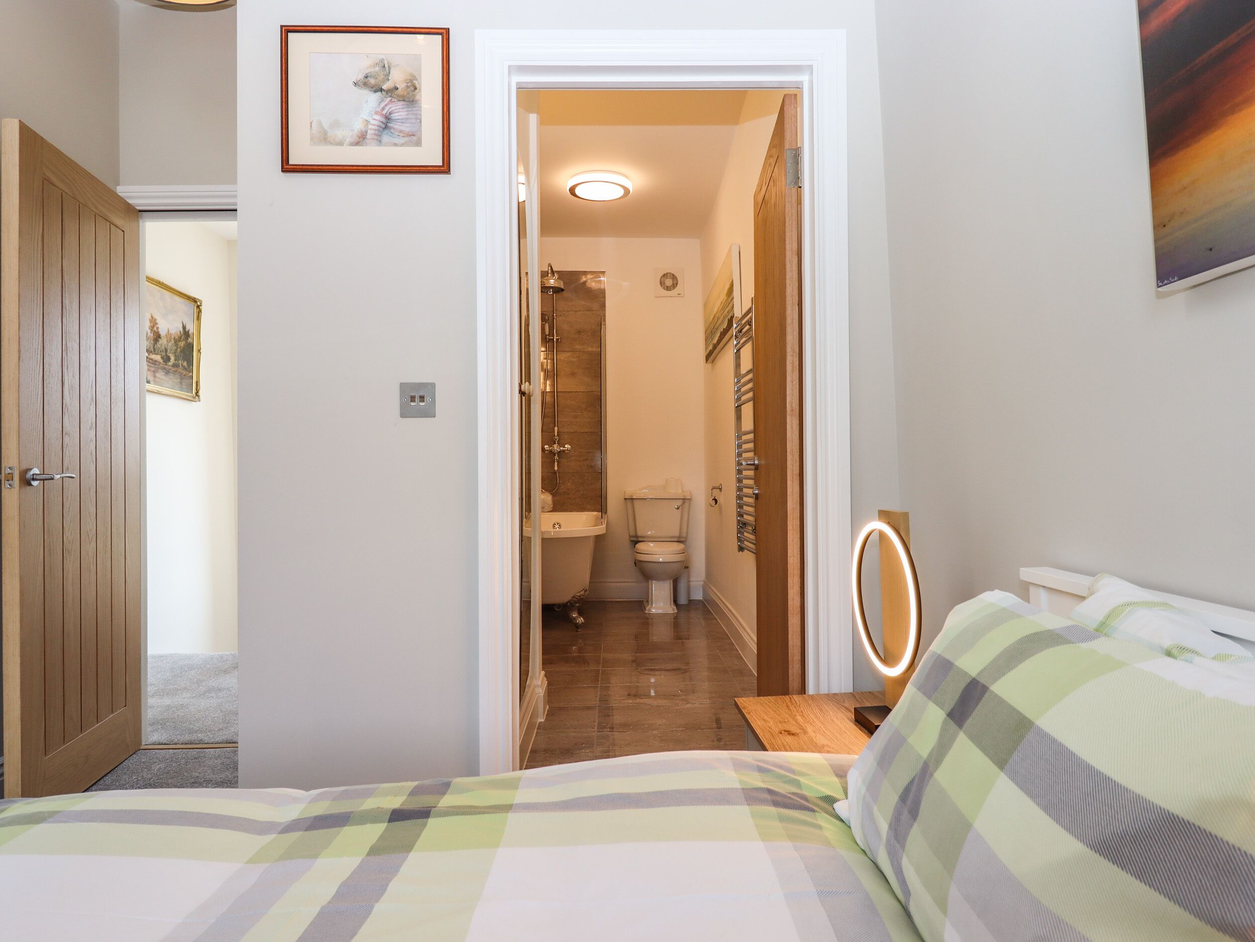 A bedroom with a bed, a bedside table with a lamp, a mirror, and a bathroom visible through an open door.