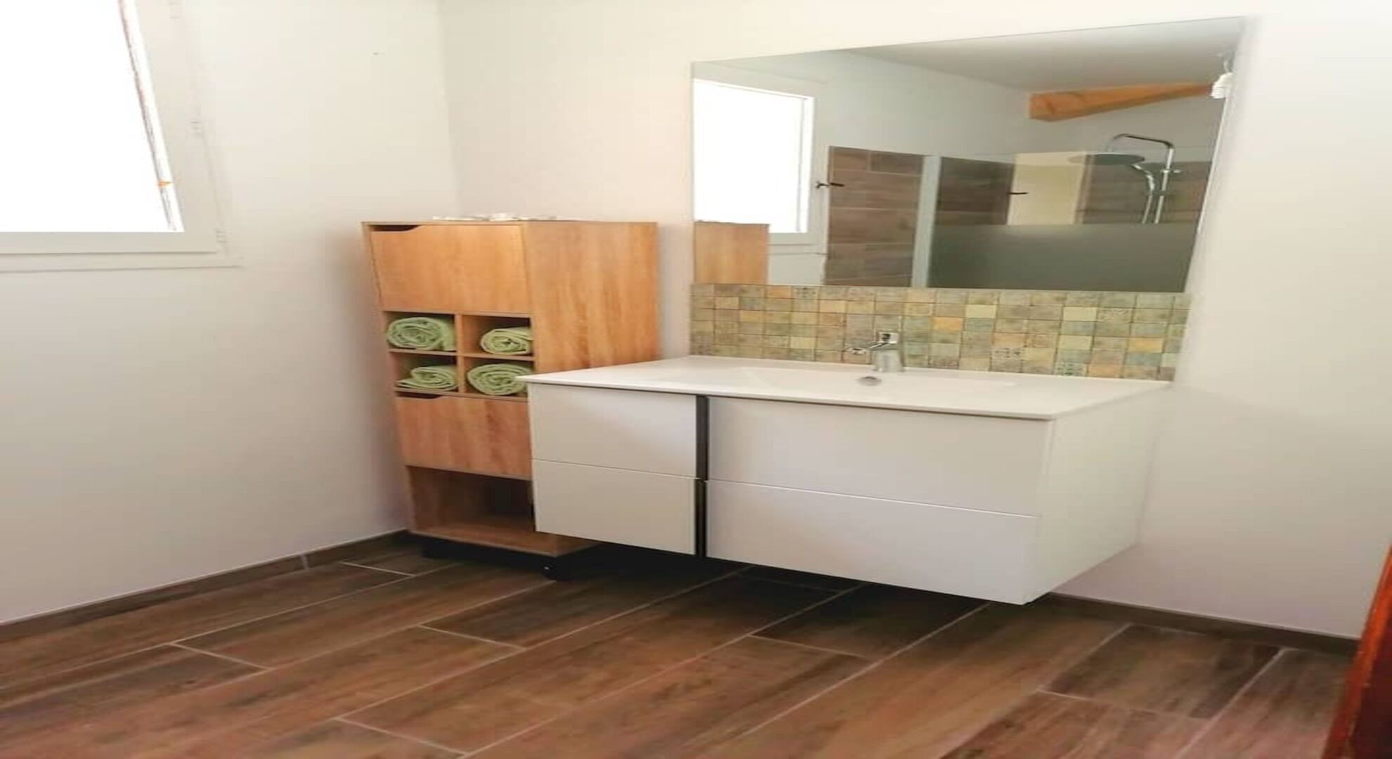 Une petite salle de bain avec un lavabo blanc, un meuble en bois et un pare-feu en carreaux.