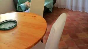 Ett rum med ett träbord, en grön soffa, en vit stol, en liten prydnad på väggen och ett fönster med gardiner.