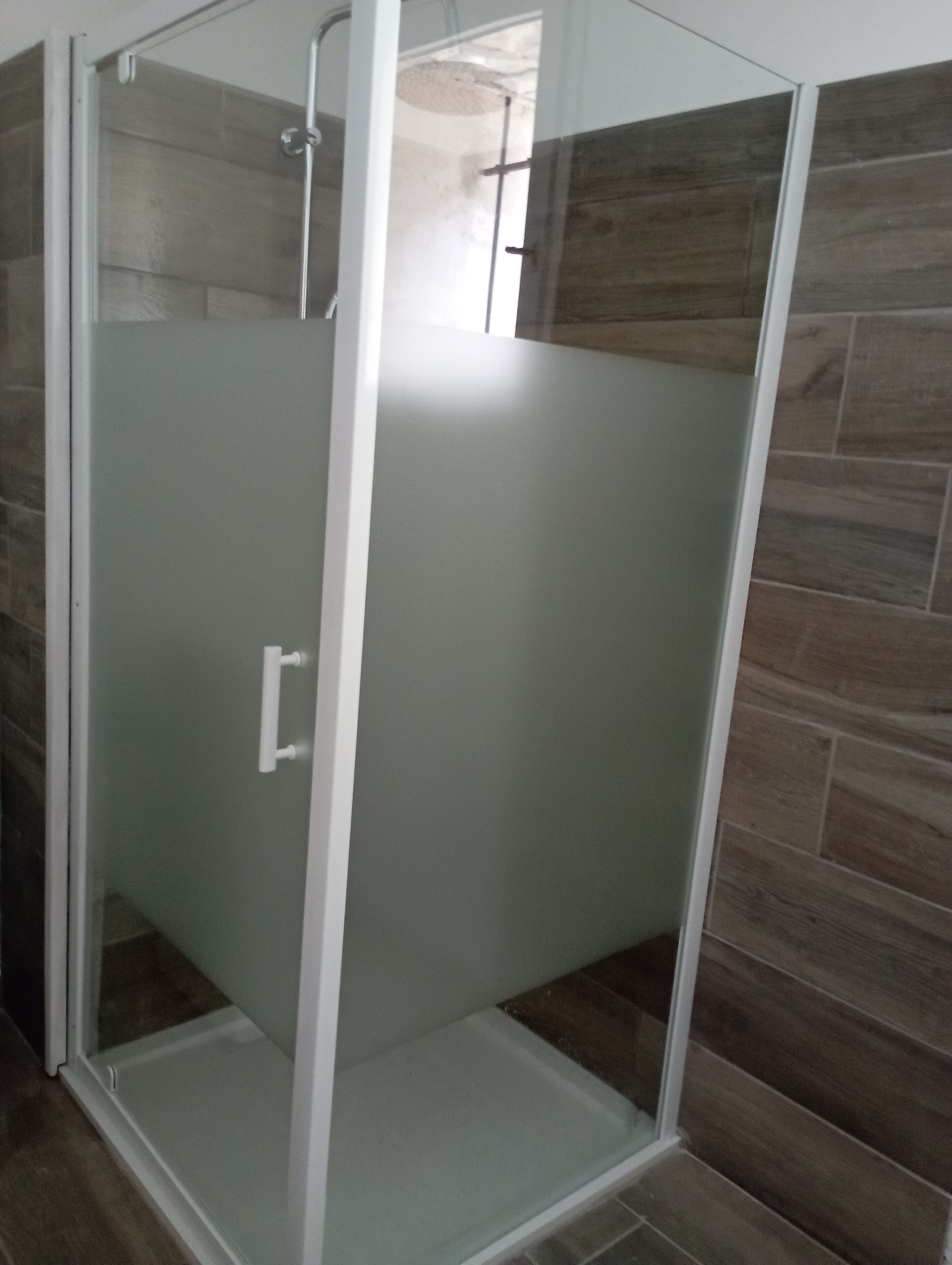 A glass-enclosed shower with a white frame, a white door, and a tiled floor.