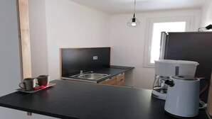 Ett kompakt kök med en svart bänkskiva, en diskho i rostfritt stål, en kaffebryggare och ett fönster som släpper in naturligt ljus.