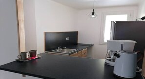 Een compacte keuken met een zwart aanrecht, een roestvrijstalen spoelbak, een koffiezetapparaat en een raam voor natuurlijk licht.