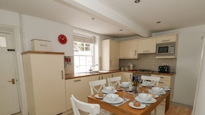 A kitchen with a dining table set for four, white chairs, a bread box, a clock, and a microwave. - Harbour Tales (Weymouth)