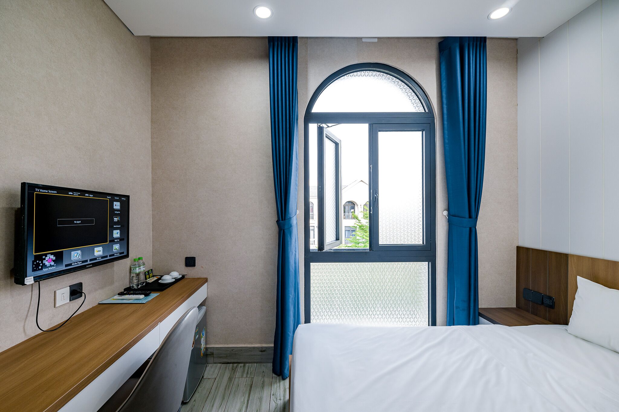 Una habitación de hotel con cama, escritorio con televisor y ventana con cortinas.
