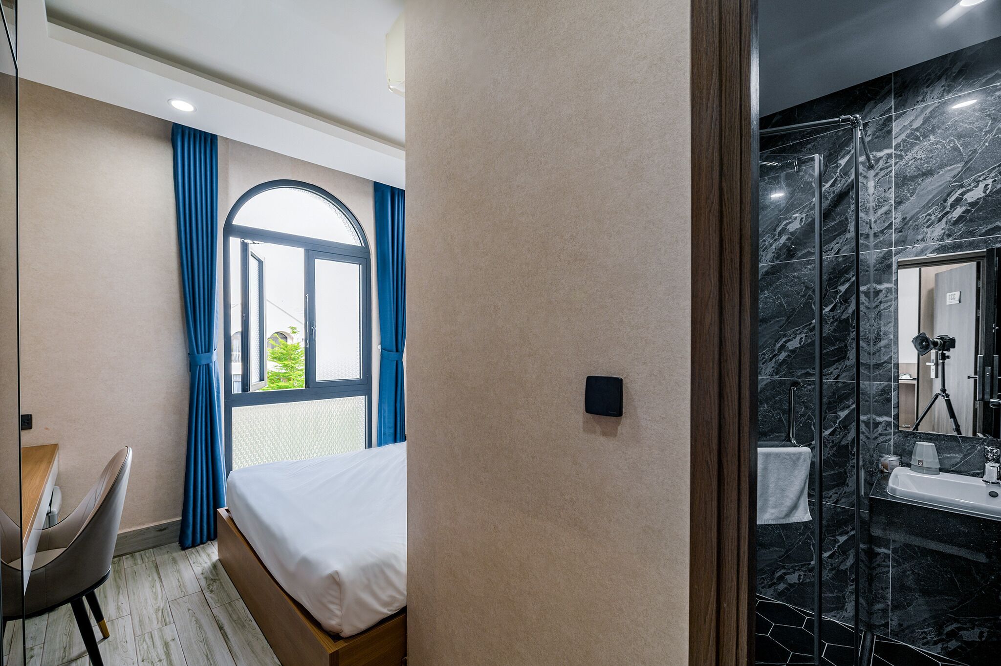 Une chambre d’hôtel comprenant un lit, un bureau, une fenêtre avec des rideaux et une salle de bain avec une douche et un miroir.