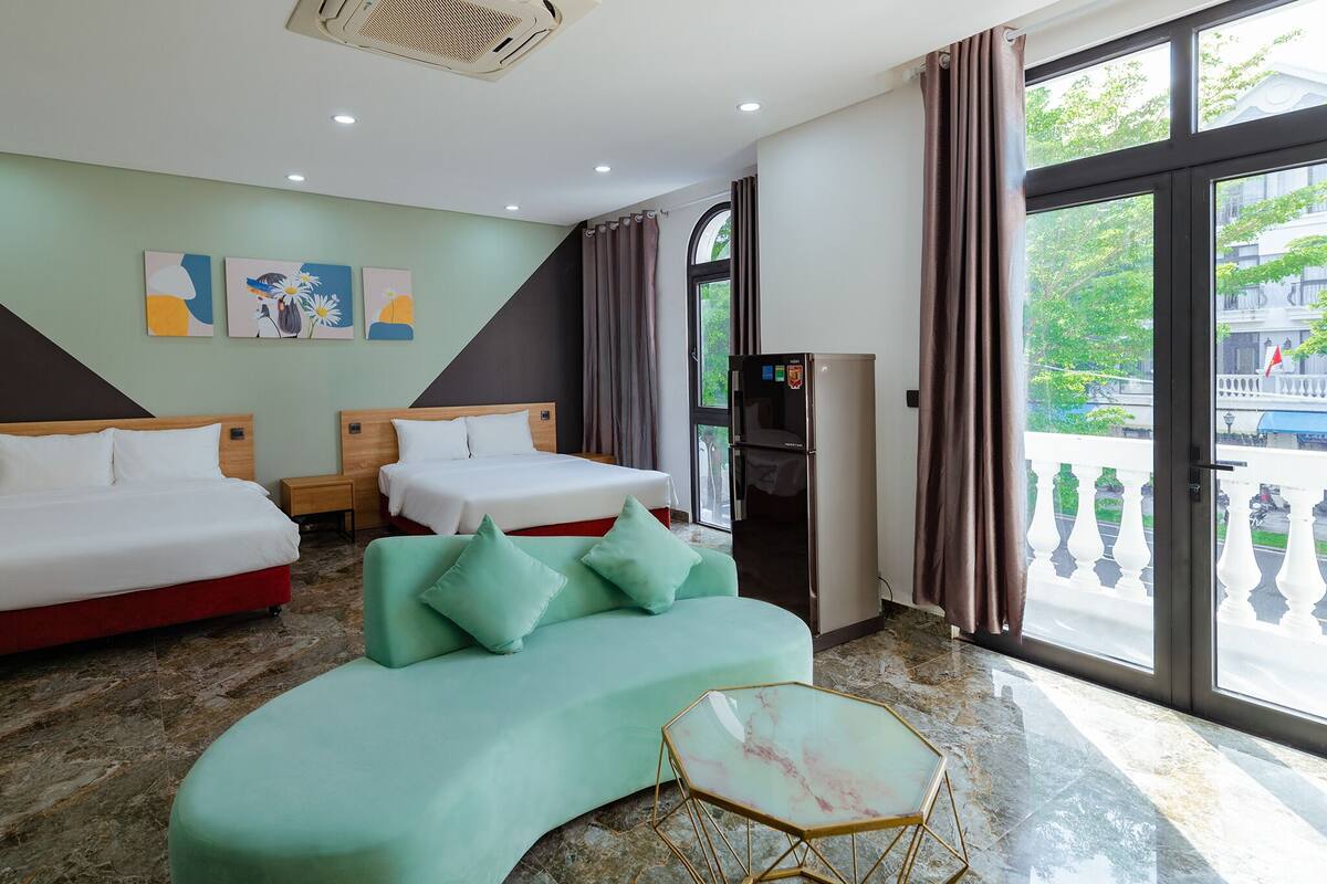 A hotel room with two beds, a sofa, a small table, and a view of the outside.