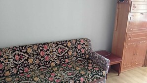 Et værelse med en sofa med blomstermønster, et træskab med skuffer og en ventilator ovenpå.