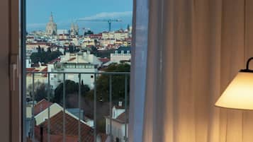 Quarto de hotel com uma grande janela que oferece vista para a paisagem urbana, incluindo edifícios históricos e uma torre imponente.