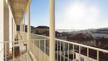 A balcony with a chair, a concrete ceiling, and a view of buildings and a bridge.