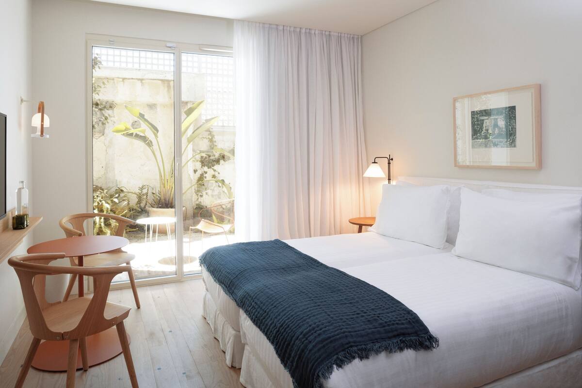 A hotel room with a bed, a desk, chairs, a window with curtains, and a framed picture on the wall.