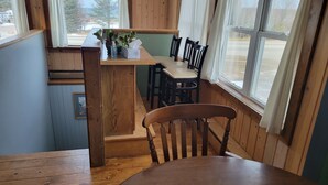 A wooden interior with a dining table, chairs, a small kitchen area, and large windows.
