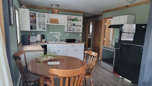 A compact kitchen with white cabinets, a black refrigerator, and a wooden dining table with chairs.