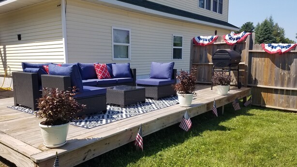 A covered patio with outdoor furniture, potted plants, and American flags.
