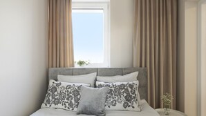Una cama impecablemente arreglada con almohadillas de estampado floral y una almohada de acento gris, un cabecero tapizado en gris y una mesita de noche con un florero.