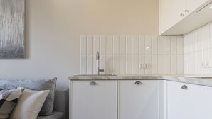 Una cocina moderna con armarios blancos, encimera de mármol y un grifo de pared.