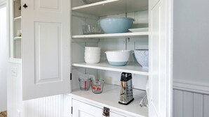 A white kitchen cabinet with open shelves containing bowls, measuring cups, and a coffee maker.