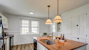 A kitchen with white cabinetry, a wooden countertop, a built-in sink, and pendant lighting.