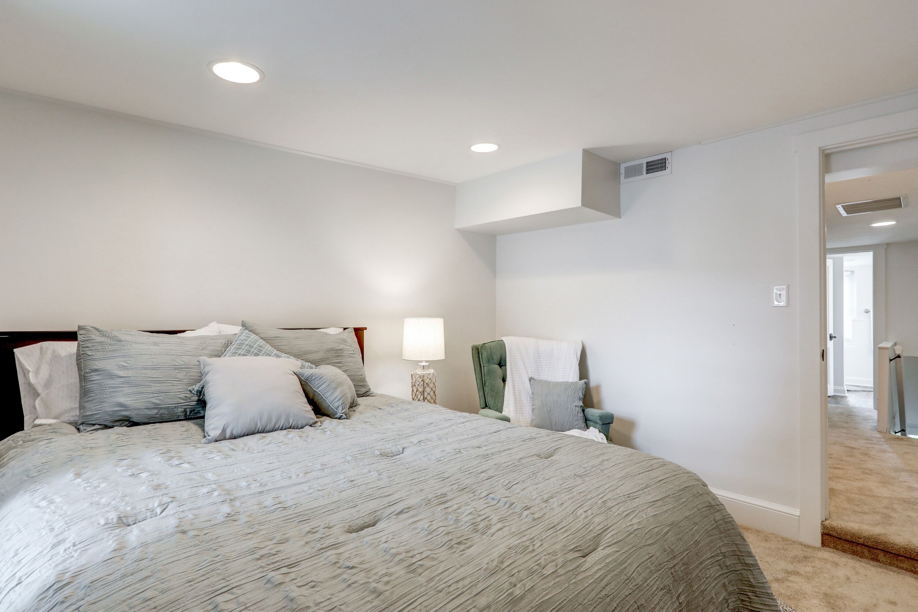 A bedroom with a large bed, a bedside table with a lamp, and a chair.