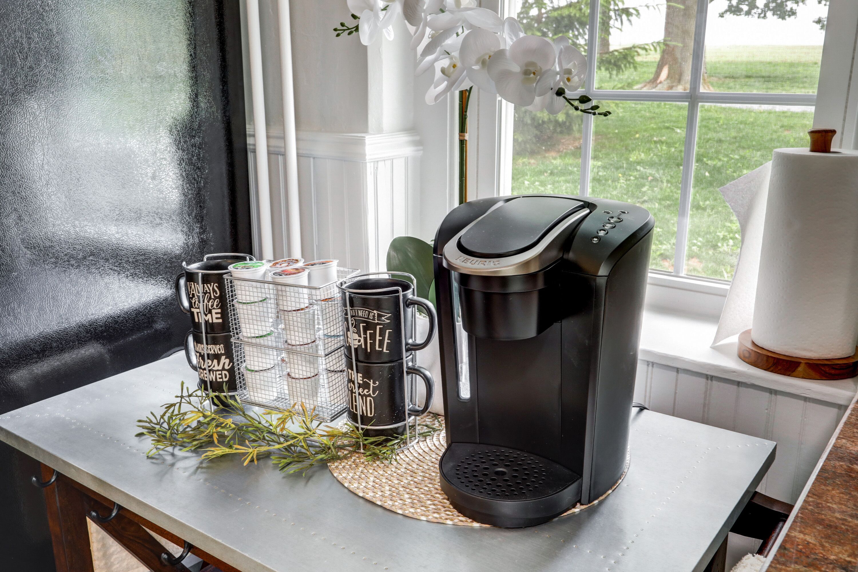 Eine Kaffeemaschine auf einem Tisch mit drei Tassen und einer kleinen Pflanze.