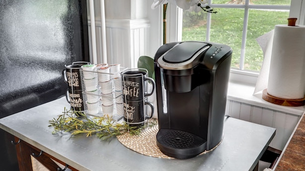 En kaffebryggare står på ett bord tillsammans med tre muggar och en liten växt.