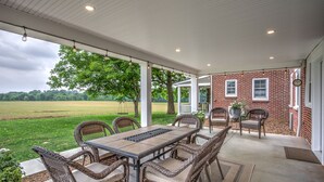 A covered patio with a table and chairs, a brick wall, and a view of a green field.
