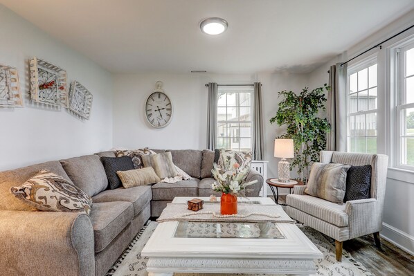 A living room with a sectional sofa, a coffee table with a vase, and a clock on the wall.
