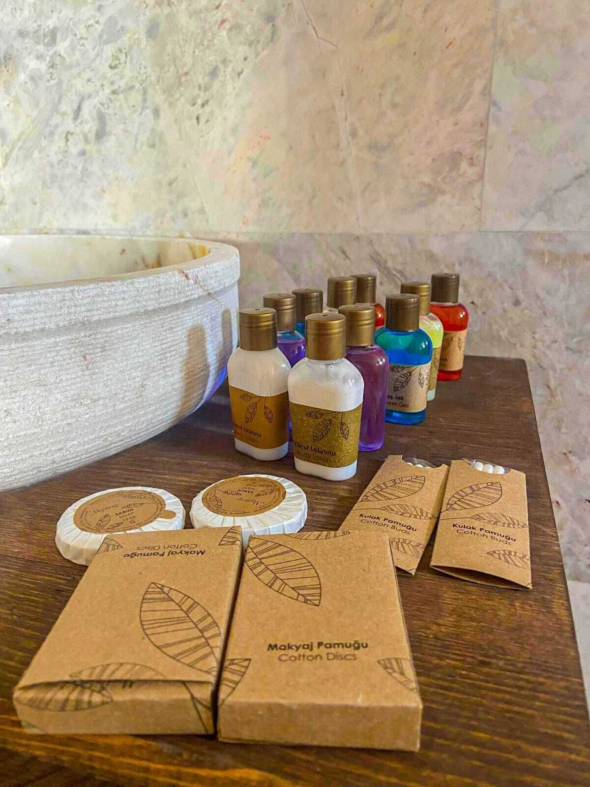 Une table en bois sur laquelle se trouvent divers objets, notamment des flacons de lotion pour le corps, des disques de coton et de petites boîtes marron étiquetées « Disques de coton MakyaJ Pamugú ».