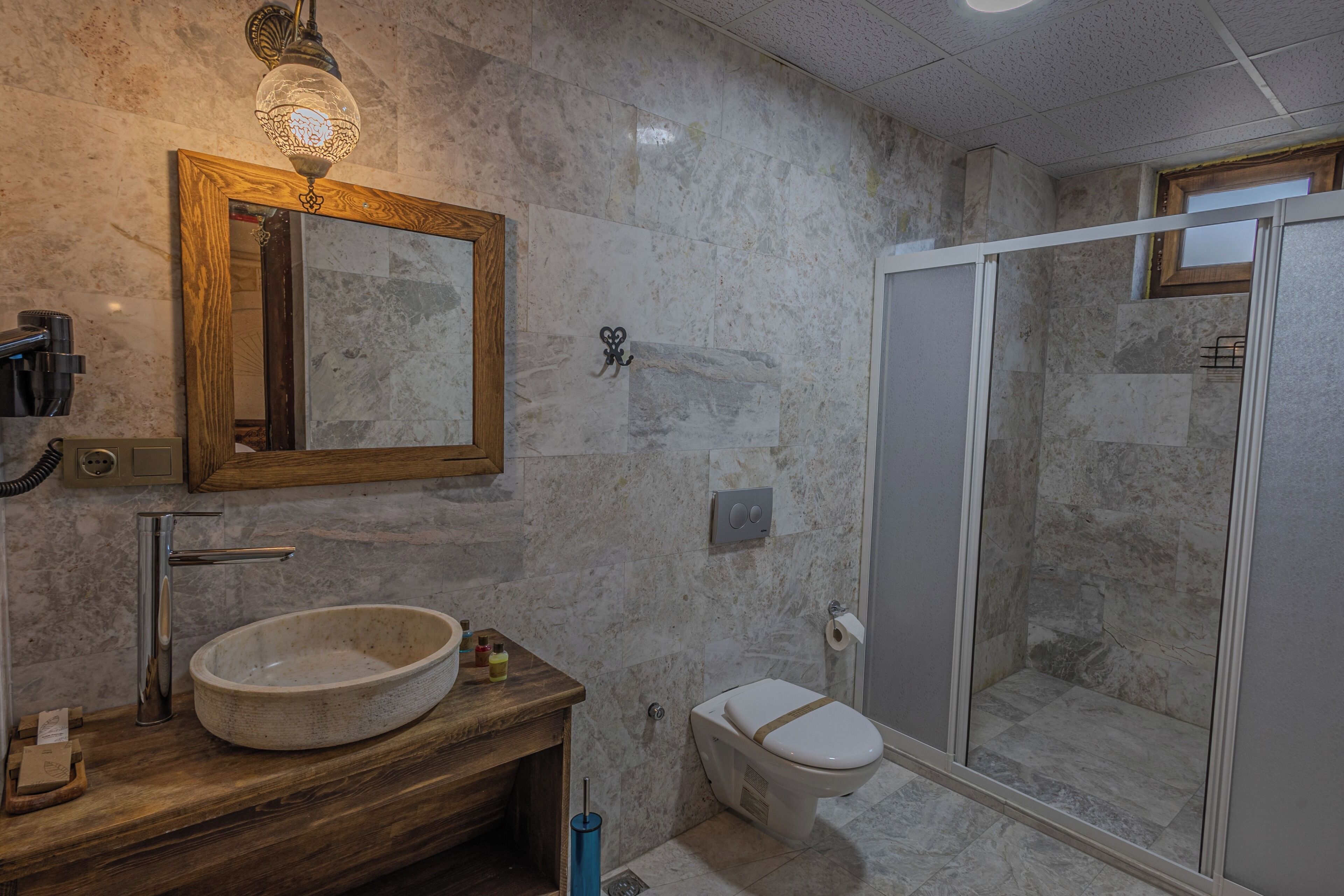 A bathroom with a wooden vanity, a marble sink, a toilet, and a glass-enclosed shower.