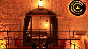 A cozy, dimly lit room with a stone wall, a wooden ceiling, and a table with chairs. A sign with the text "Cappadocia" is visible on the wall. - Cordial Cappadocia Hotel (Ürgüp)