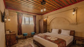 A bedroom with a wooden bed, a desk, a chair, a wardrobe, and a patterned rug. - Cordial Cappadocia Hotel (Ürgüp)