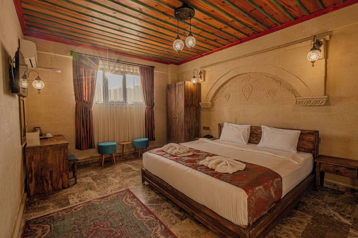 A bedroom with a wooden bed, a desk, a chair, a wardrobe, and a patterned rug.