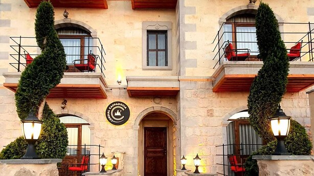 A building with a central entrance, multiple balconies with red chairs, and stone pillars with lights. - Cordial Cappadocia Hotel (Ürgüp)