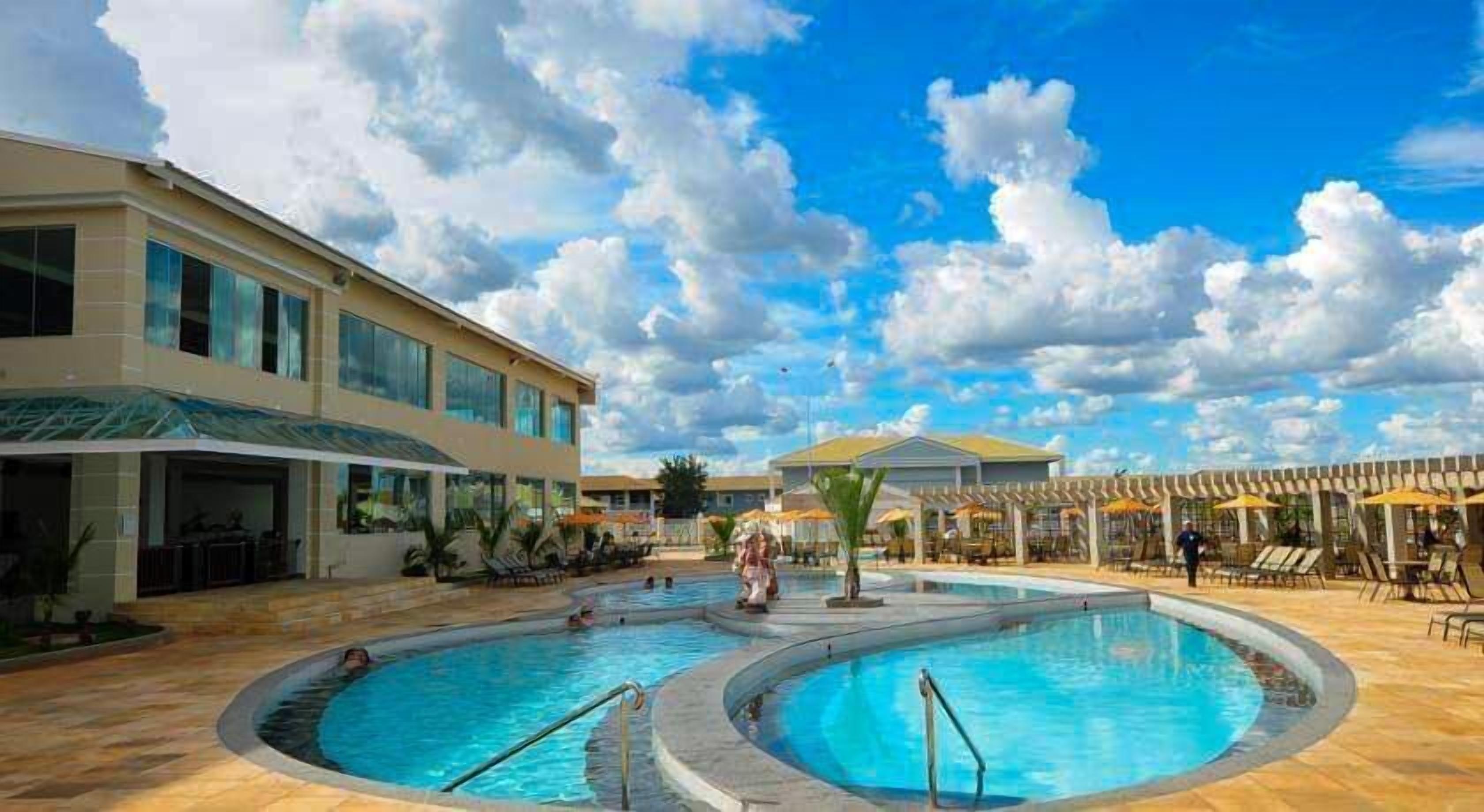 Um hotel com área de piscina, incluindo duas piscinas circulares e um espaço coberto com assentos e guarda-sóis.