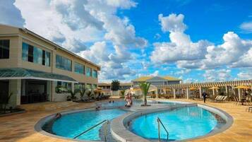 Um hotel com área de piscina, incluindo duas piscinas circulares e um espaço coberto com assentos e guarda-sóis.