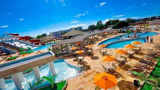 Área de piscina de un resort con varias piscinas, sillones reclinables y sombrillas.