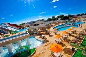 Área de piscina de un resort con varias piscinas, sillones reclinables y sombrillas.