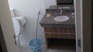 Un baño con azulejos blancos, un lavabo con espejo, un inodoro y un cubo de basura azul.
