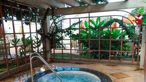 Un jacuzzi rodeado por una cerca metálica, con plantas y mobiliario exterior al fondo.