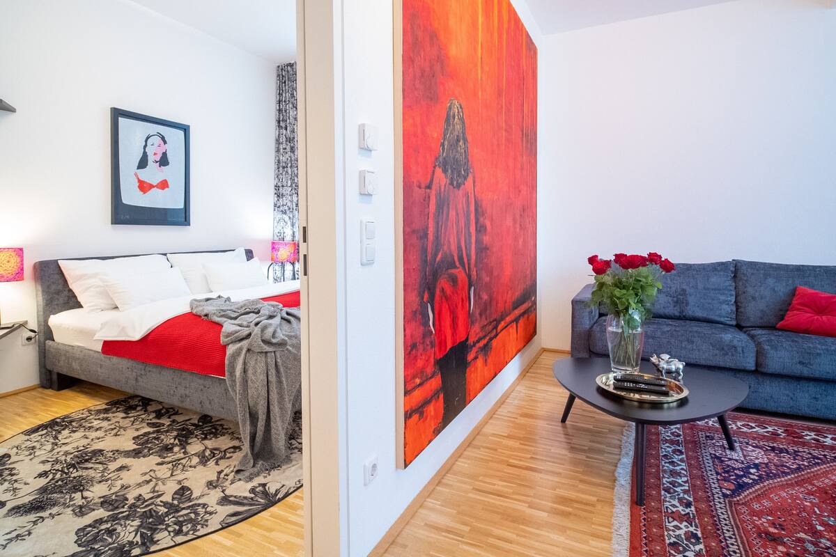 A modern living room with a bed, a sofa, a coffee table, and a large abstract painting on the wall.