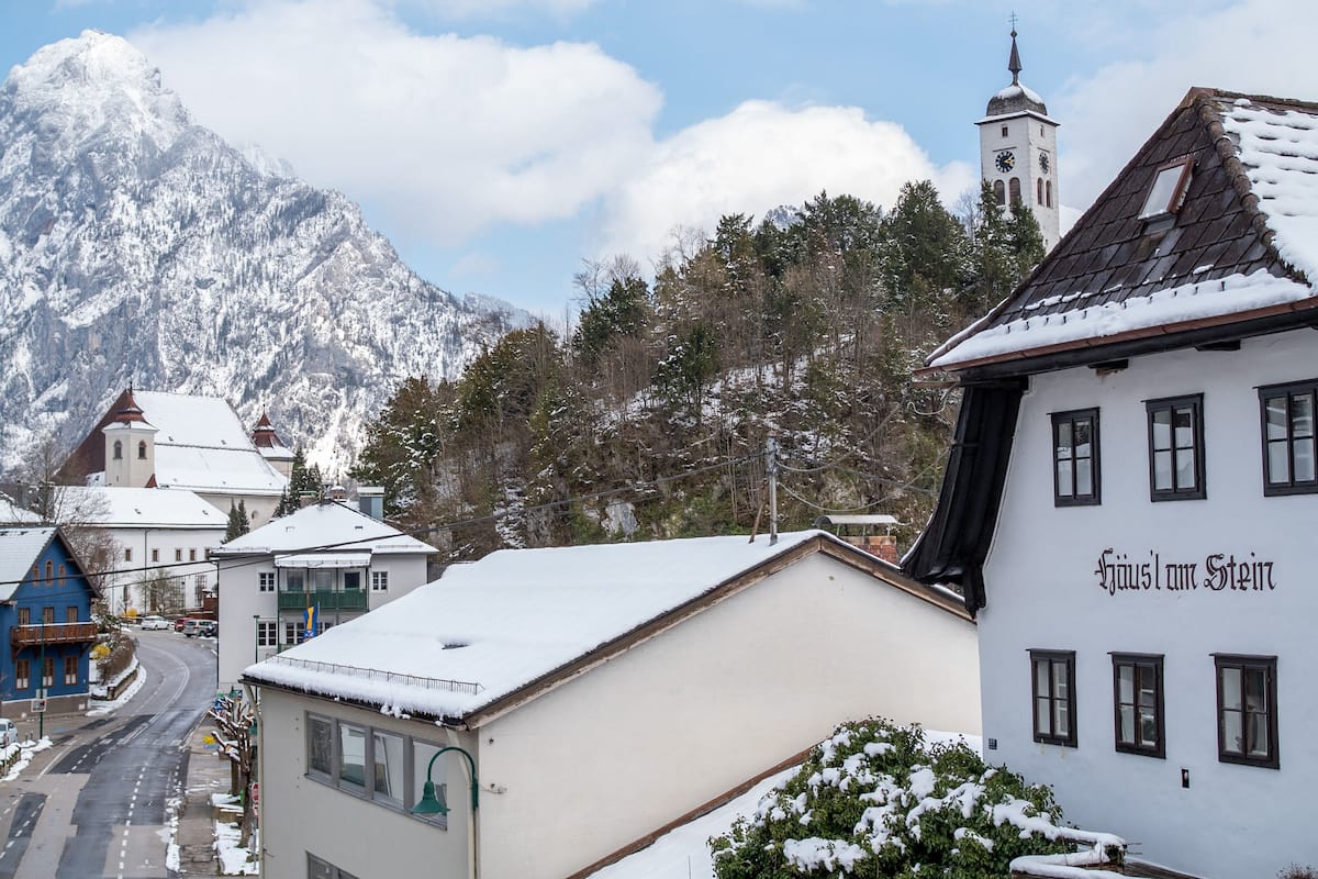 A snow-covered mountain village with traditional buildings, including a church with a clock tower.