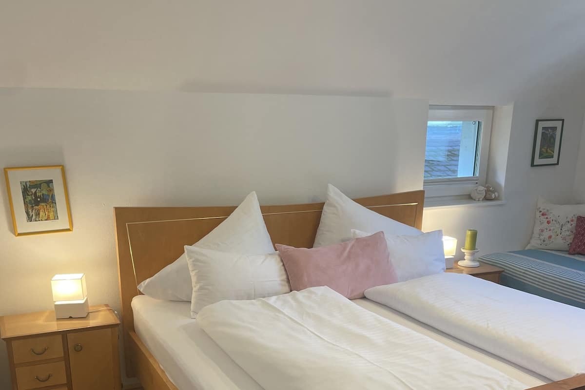 A neatly made bed with white and pink pillows, a wooden headboard, and a bedside table with a lamp.