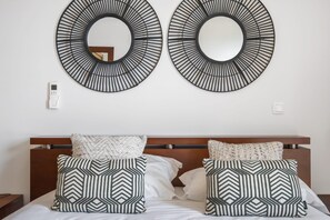 Una habitación de hotel con cabecera de madera, dos espejos grandes en la pared y almohadas estampadas.